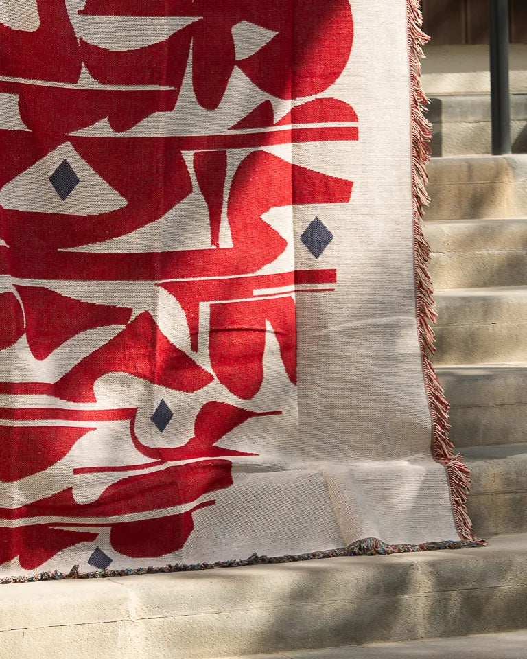 Calligraforms Throw by Wissam Shawkat — woven blanket with bold red Arabic letterforms on neutral ground and fringe edges