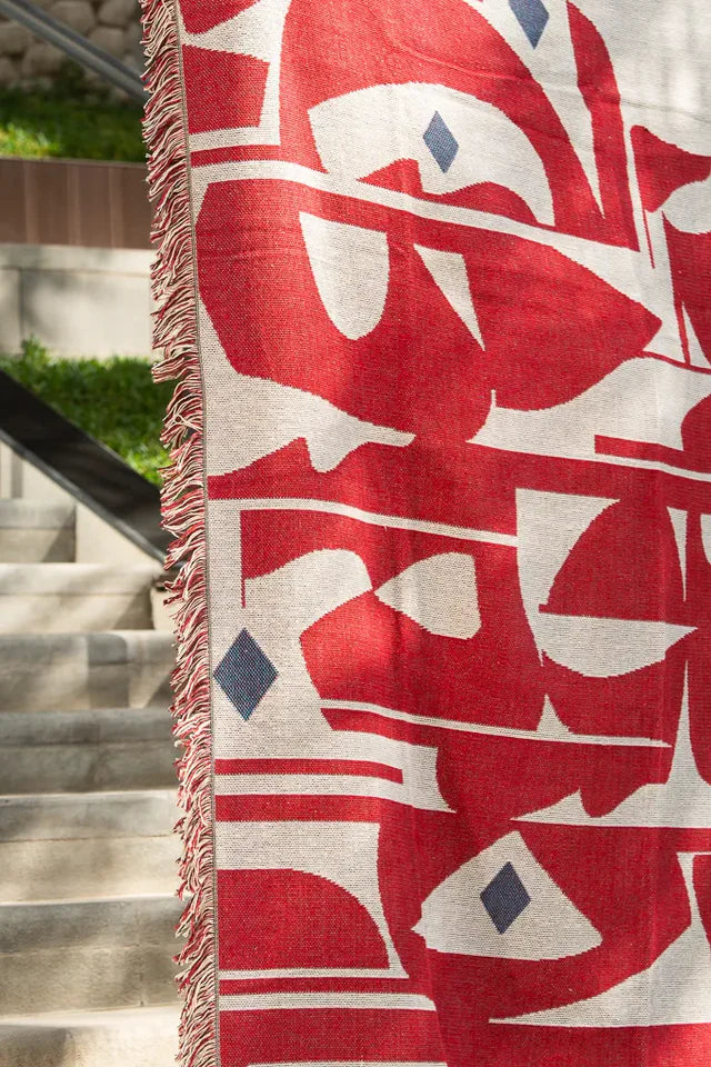 Calligraforms Throw by Wissam Shawkat — woven blanket with bold red Arabic letterforms on neutral ground and fringe edges