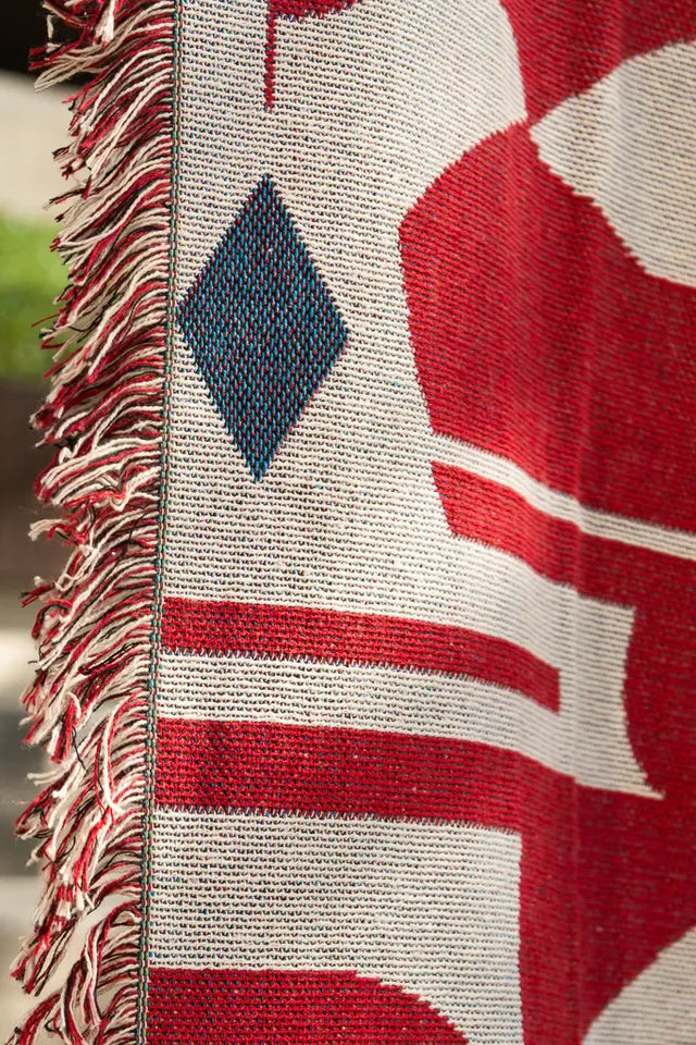 Calligraforms Throw by Wissam Shawkat — woven blanket with bold red Arabic letterforms on neutral ground and fringe edges