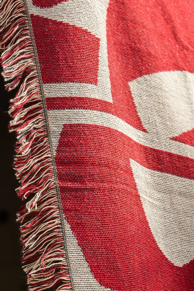 Calligraforms Throw by Wissam Shawkat — woven blanket with bold red Arabic letterforms on neutral ground and fringe edges