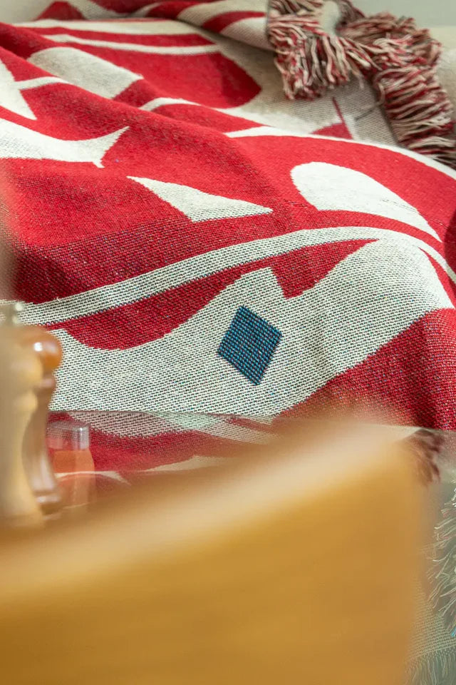 Calligraforms Throw by Wissam Shawkat — woven blanket with bold red Arabic letterforms on neutral ground and fringe edges