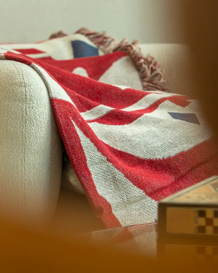 Calligraforms Throw by Wissam Shawkat — woven blanket with bold red Arabic letterforms on neutral ground and fringe edges