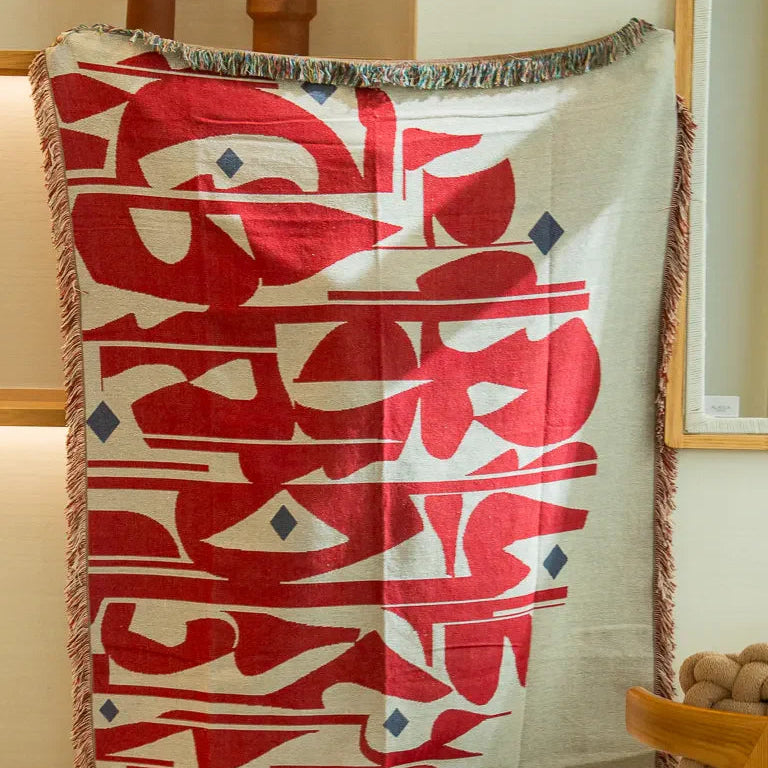 Calligraforms Throw by Wissam Shawkat — woven blanket with bold red Arabic letterforms on neutral ground and fringe edges